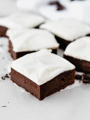 guinness brownie with vanilla bean cream cheese frosting in front of more brownies on a piece of parchment.