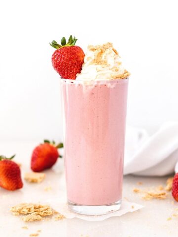 healthy strawberry cheesecake smoothie in a glass topped with whipped cream, graham cracker crumbs and a strawberry.