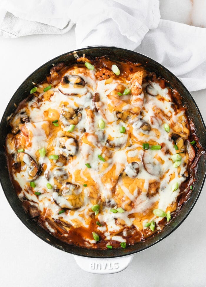 BBQ Mushroom Chicken topped with cheese and green onions in a white skillet with a napkin around the handle.
