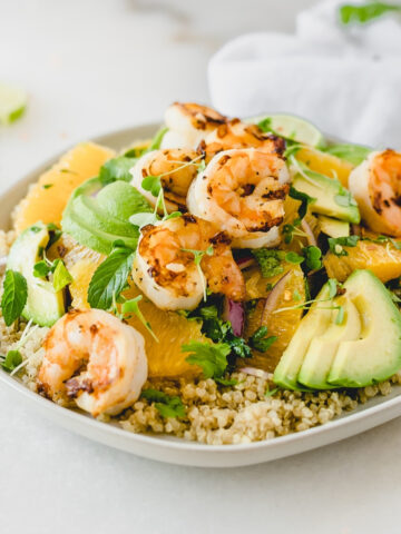 Shrimp, Orange and Avocado Quinoa Salad topped with herbs on a grey plate.