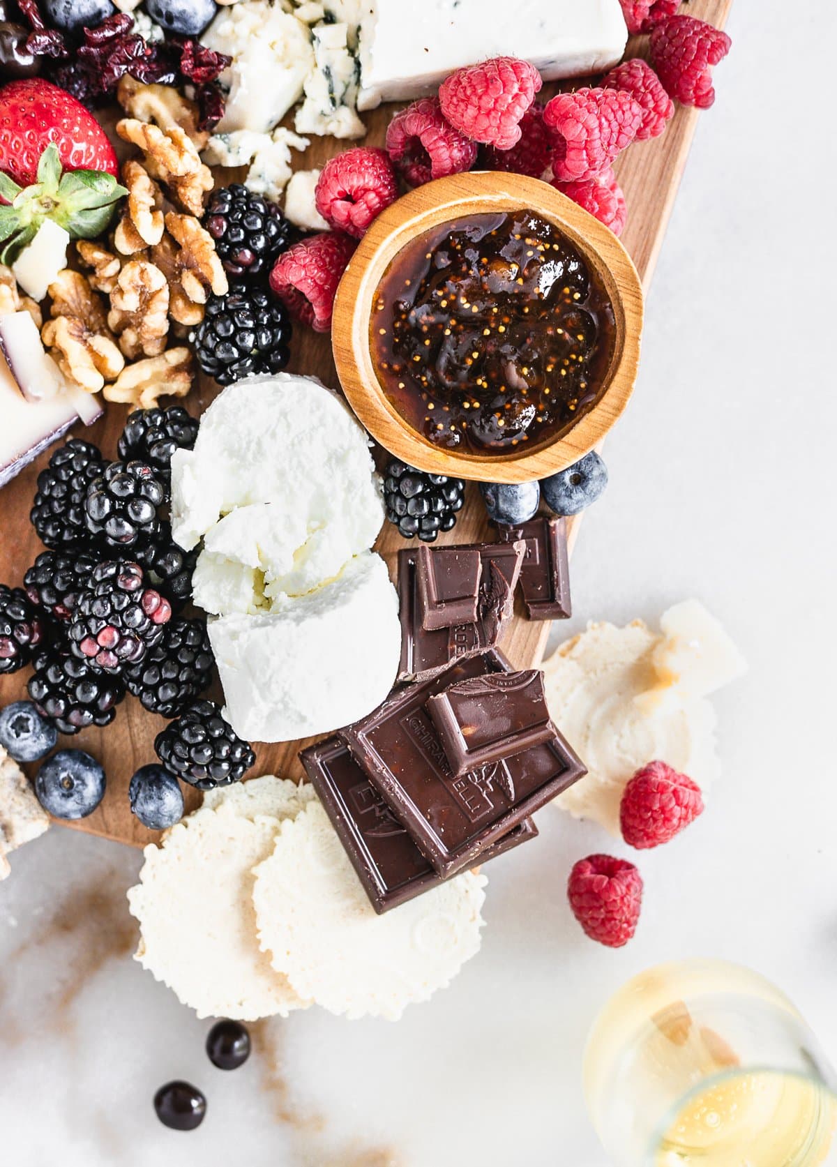 closeup of goat cheese, berries, nuts, fig jam and chocolate on a cheese board.