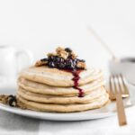 blueberry muffin pancakes topped with blueberries and granola on a white plate with a gold fork next to it.