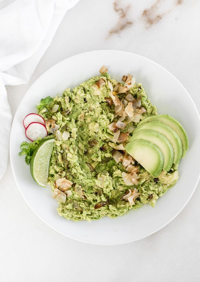 Caramelized onion guacamole on a plate with lime and sliced avocado.
