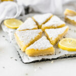 lavender lemon bars cut into triangles on a wire rack surrounded by lemon slices.