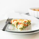 slice of kale red pepper and feta frittata on a white plate with a black fork.