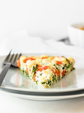 slice of kale red pepper and feta frittata on a white plate with a black fork.