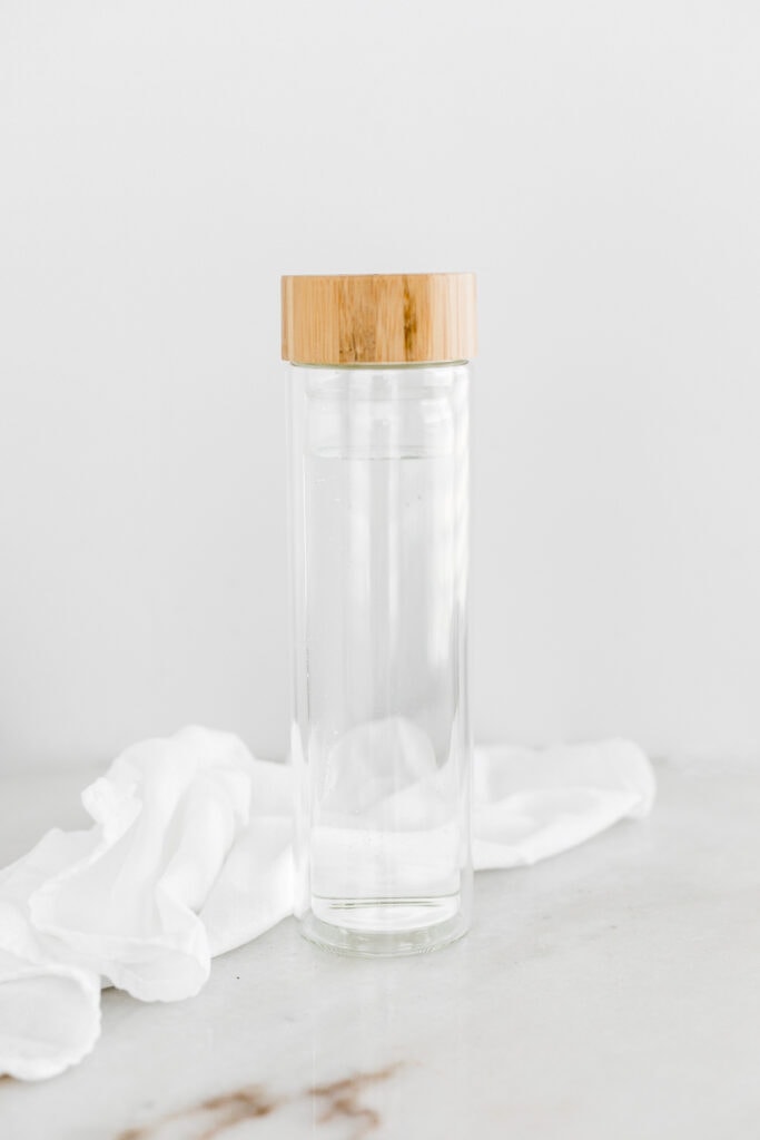 glass water bottle with wooden lid with a white napkin behind it.