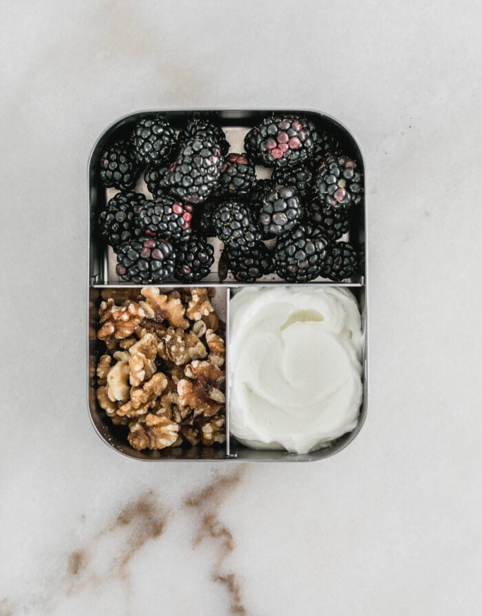 bento box with berries, walnuts and yogurt in it.