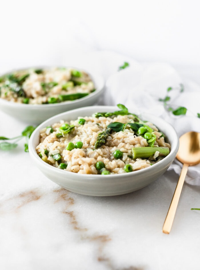 spring vegetable brown rice risotto in a grey bowl with a gold spoon beside it.