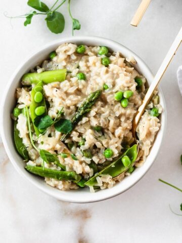spring vegetable brown rice risotto in a bowl with a gold spoon in it.