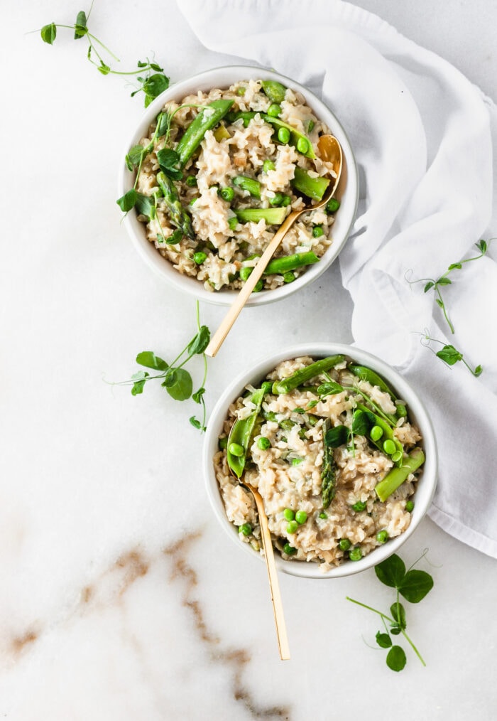 overhead view of two bowls of spring vegetable brown rice risotto with gold spoons in them.