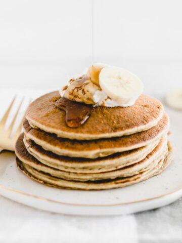 a stack of banana chai pancakes topped with yogurt and bananas on a white plate.