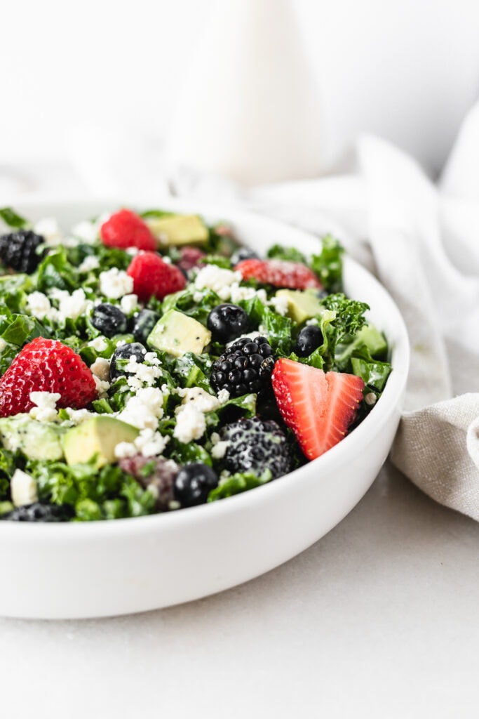 closeup of a berry avocado kale salad in a white bowl.