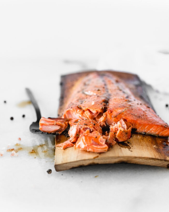 grilled bourbon glazed salmon on a cedar plank with a black fork cutting away a piece.