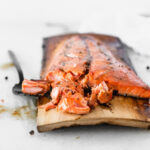 grilled bourbon glazed salmon on a cedar plank with a black fork cutting away a piece.