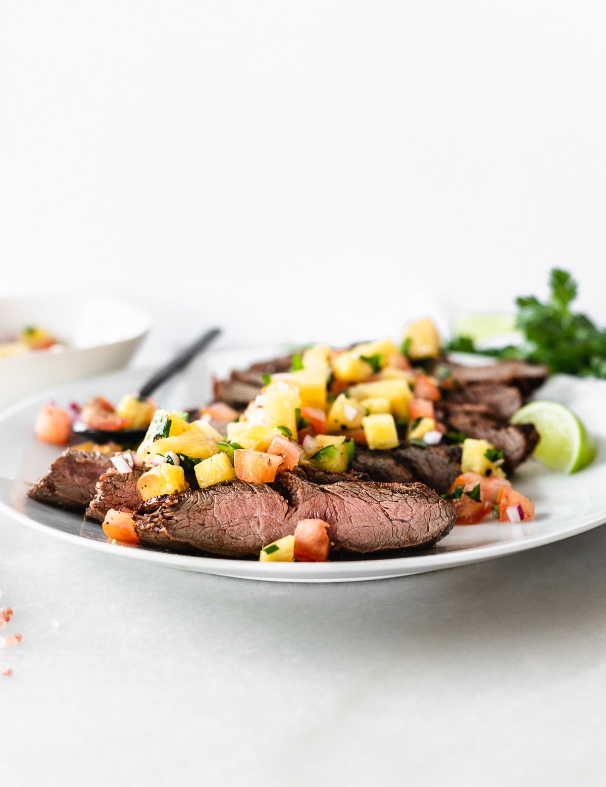closeup of sliced chipotle flank steak topped with pineapple salsa on a white plate.