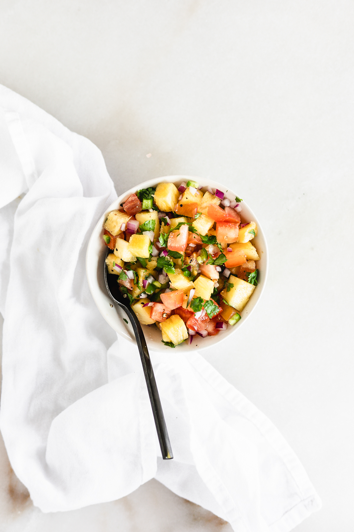 overhead view of pineapple salsa in a white bowl with a black spoon in it.