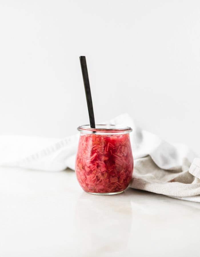 glass jar of vanilla bean rhubarb compote with a black spoon in it.