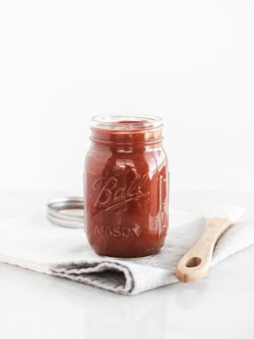 Homemade Texas style barbecue sauce in a glass jar on top of a gray and white napkin.
