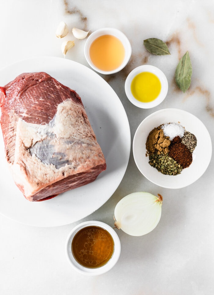 overhead view of ingredients needed to make barbacoa beef on a white marble background.