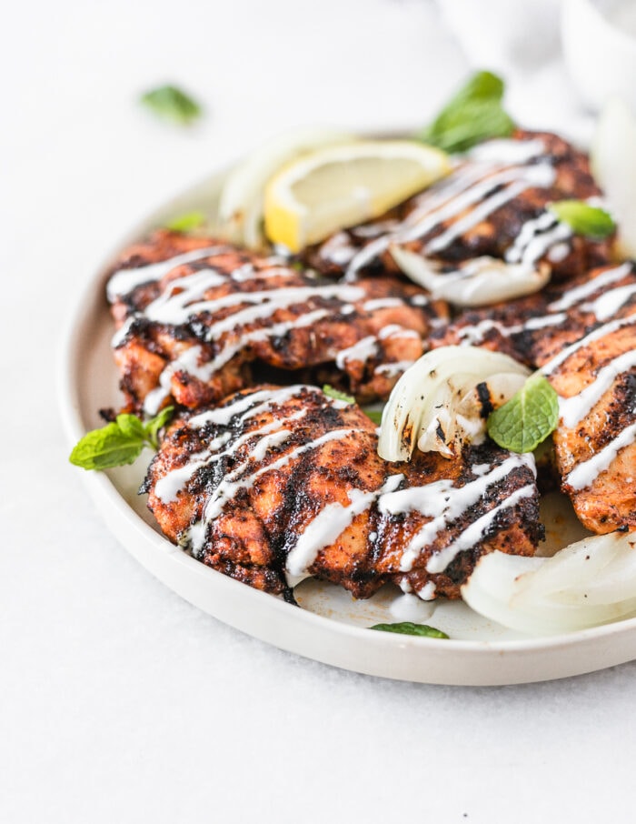 harissa grilled chicken thighs and onions with lemon mint yogurt sauce drizzled over them on a white plate.