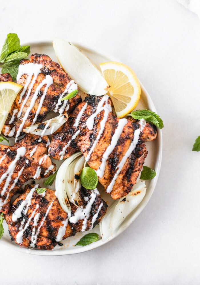 overhead view of harissa grilled chicken thighs with lemon mint yogurt sauce drizzled over the top.