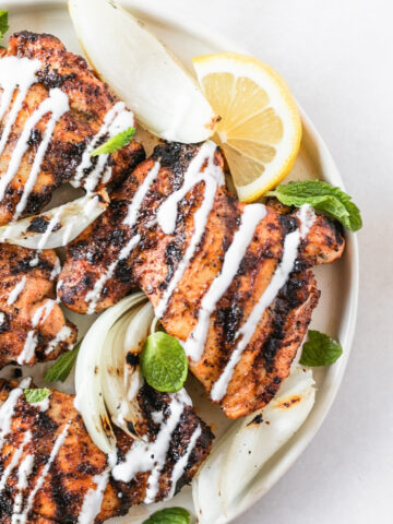 overhead view of harissa grilled chicken thighs with lemon mint yogurt sauce drizzled over the top.
