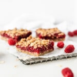 Raspberry Oat Crumble Bars on a wire cooling rack with oats and raspberries scattered around them.