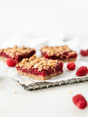 Raspberry Oat Crumble Bars on a wire cooling rack with oats and raspberries scattered around them.