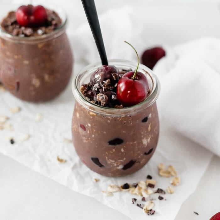 black forest overnight oats in a glass jar with a cherry and cacao nibs on top.