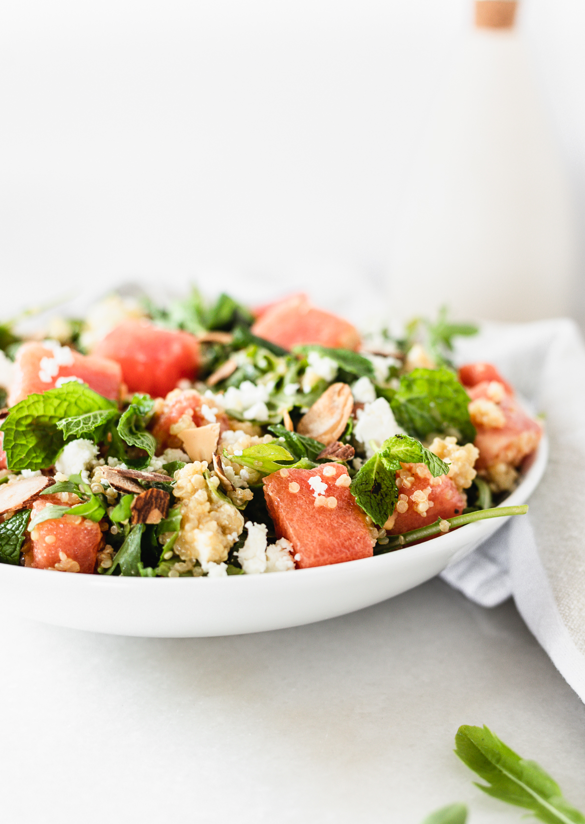 closeup of watermelon arugula grain salad with feta and mint in a white bowl.