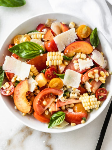 overhead view of corn peach and tomato salad in a white bowl with a black spoon beside it.