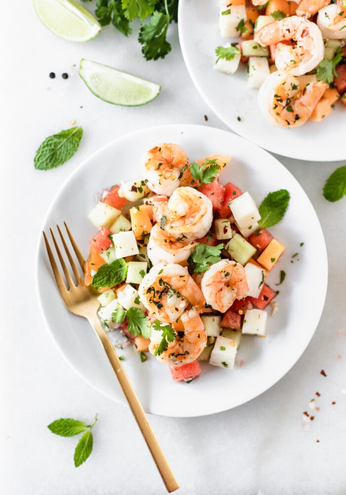 overhead view of grilled shrimp and jicama melon salad on a white plate with a gold fork.