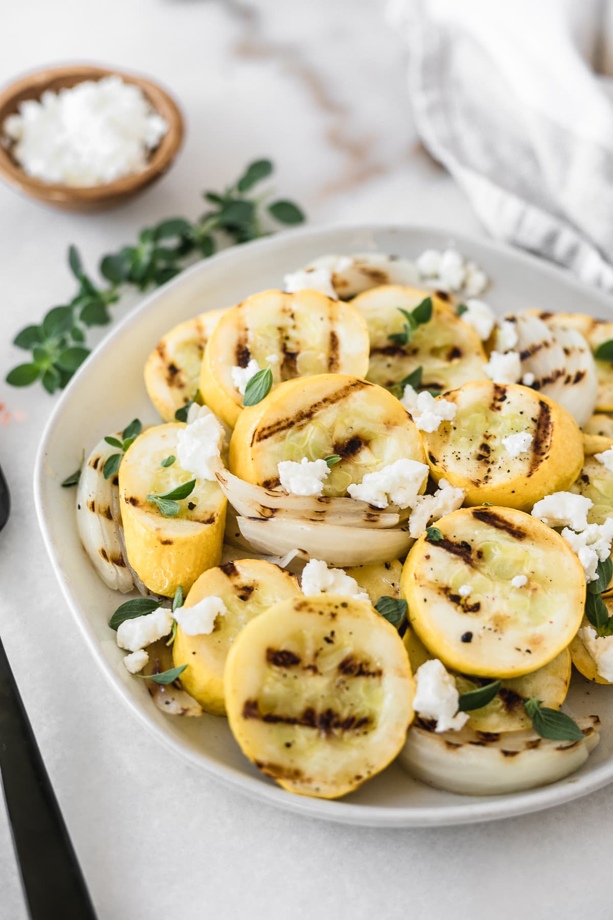 closeup of grilled summer squash and onions with goat cheese and oregano on a plate.