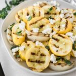 closeup of grilled summer squash and onions with goat cheese and oregano on a plate.