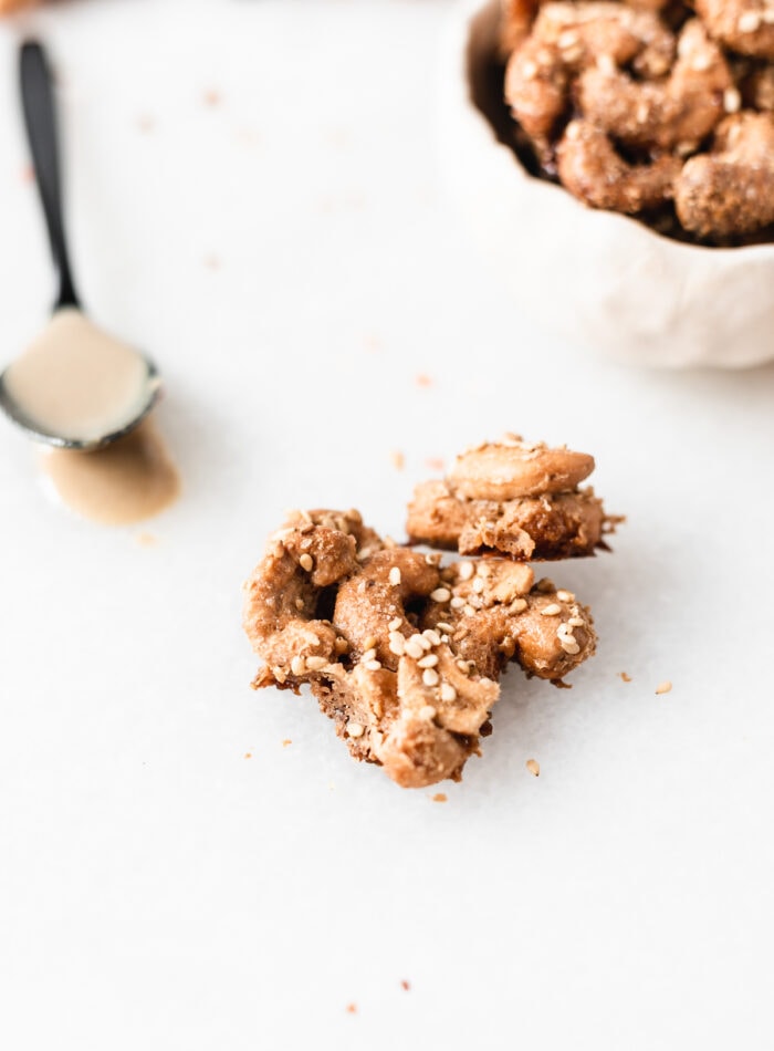 closeup of a maple tahini cashew cluster with a bowl of clusters and a spoonful of tahini in the background.