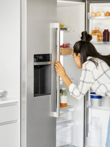 woman in a black and white shirt bending to look in the refrigerator.