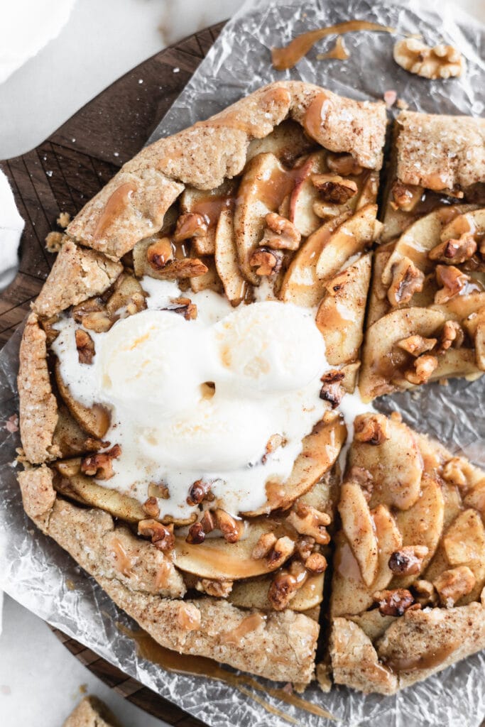 overhead view of a sliced caramel apple walnut galette with ice cream on top with one slice taken out.