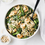 overhead view of a bowl of shrimp and broccoli pesto pasta almondine with a black serving fork in it..