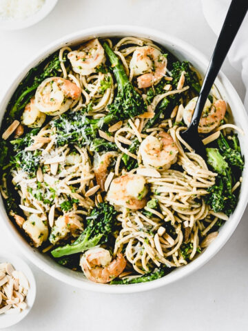 overhead view of a bowl of shrimp and broccoli pesto pasta almondine with a black serving fork in it..