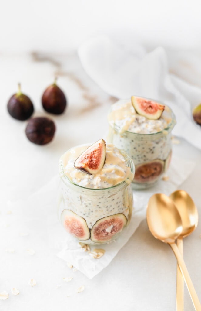 two jars of maple tahini fig overnight oats with two gold spoons beside them.