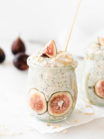 maple tahini fig overnight oats in a glass jar with a gold spoon in it with fresh figs in the background,