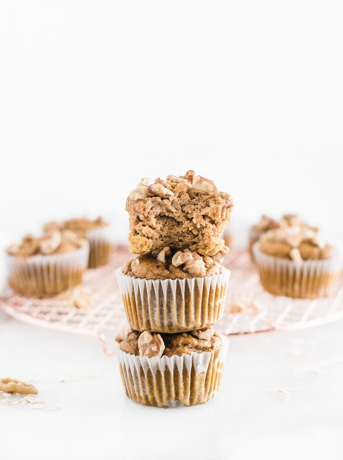 three maple walnut pumpkin muffins stacked on top of each other, the top muffin has a bite taken out.