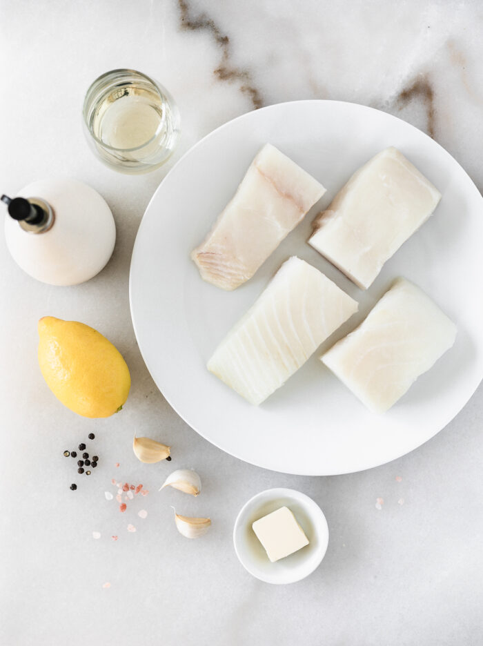 overhead view of ingredients needed to make pan seared halibut on a white marble backdrop.