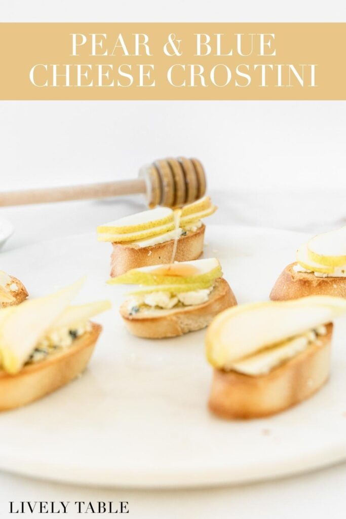 honey being drizzled over pear and blue cheese crostini on a white serving board with text overlay.