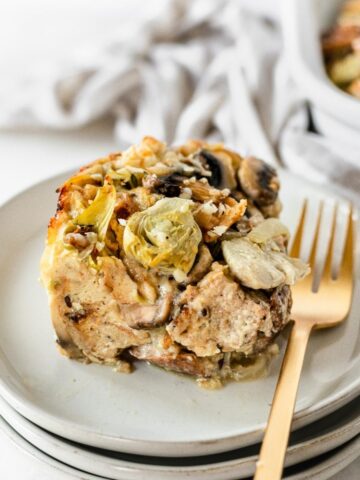 slice of Mushroom Artichoke Strata with a gold fork on a stack of plates.