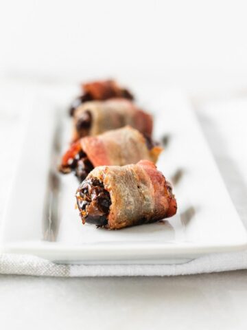 bacon wrapped dates in a line on a white tray.