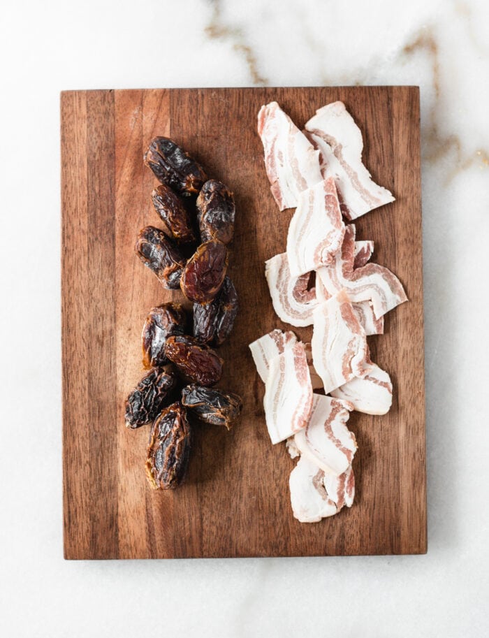 Overhead view of dates and pieces of bacon on a cutting board.