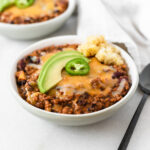 chipotle apple turkey chili topped with cheese, avocado and jalapeño in a grey bowl.