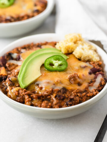 chipotle apple turkey chili topped with cheese, avocado and jalapeño in a grey bowl.
